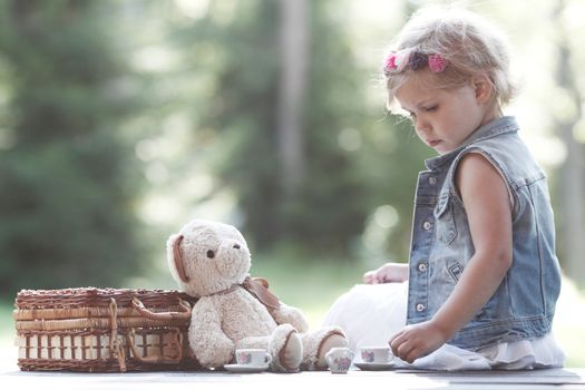 Pretty girl playing with teddy bear outdoors