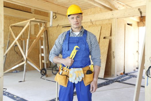 Workman with wrench inside wooden house under construction