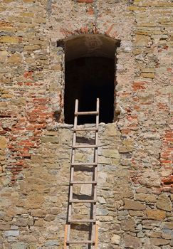 Wooden ladder next to empty window of old vintage stone wall of medieval building