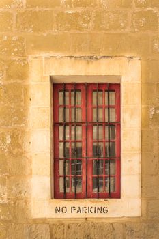 Window of a stone house with a lighter frame and a grid. No parking instruction on the frame. Former capital Mdina at the mediterranean island Malta.