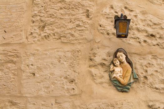 Small statue of Virgin Mary and a Child under a lantern on a texture wall of a house at the mediterranean island Malta.