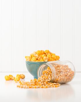 Jar of raw popcorn kernels with a bowl of popped corn in the background.