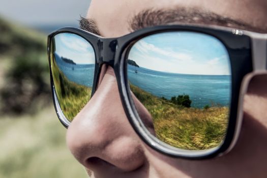 Tropical lanscape reflected in young man's sunglasses