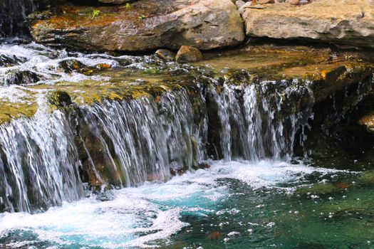 A garden pond supports a multi-tiered waterfall with many layers of rock slabs.