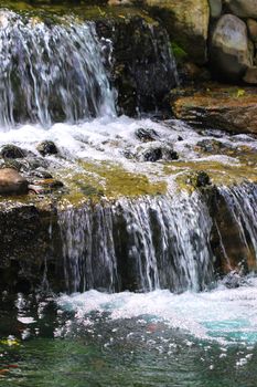 A garden pond supports a multi-tiered waterfall with many layers of rock slabs.