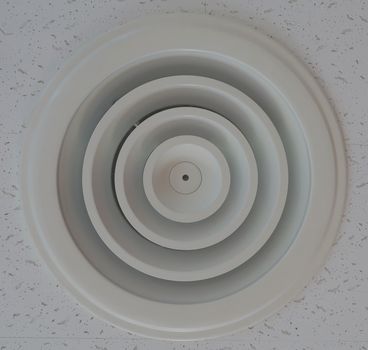 Circular shape of plastic air vent in white ceiling at office.