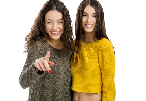 Studio portrait of two beautiful girls pointing and looking to the camera