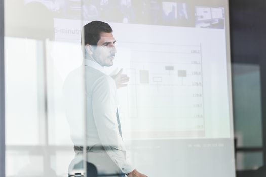 Business man making a presentation in front of whiteboard. View through glass.