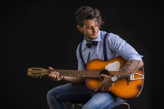 Portrait of hipster playing guitar against black background, in studio shot