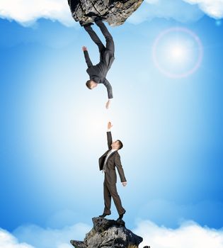 Two businessmen on rocks attracted to each other isolated on blue sky background