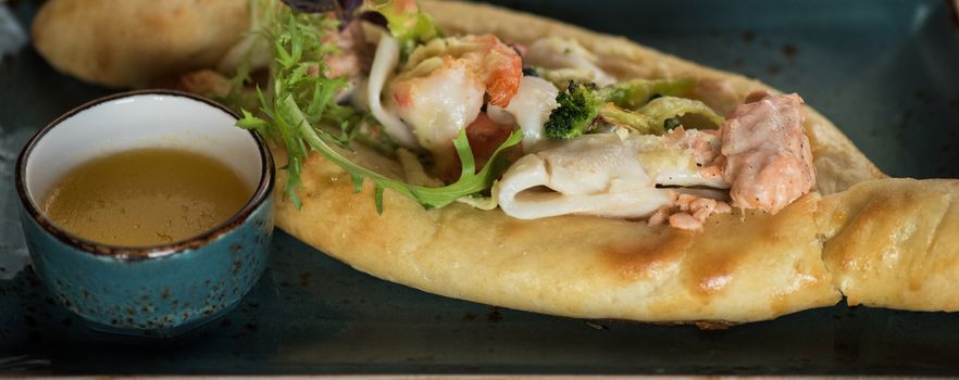 Georgian dish khachapuri with seafood and fresh vegetables close-up