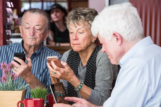 Mature friends in a coffee house distracted by their devices