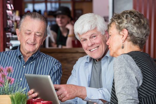 Cheerful man with mature friends on wifi with their tablet computer in a coffee house