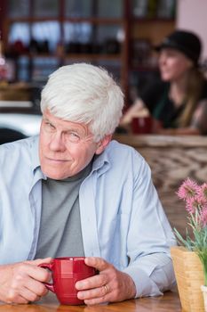 Grumpy mature man in a coffee house hunched over at table