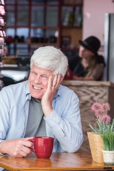 Amused mature man sitting at table with red cup in a coffee house