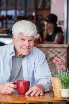 Happy mature man sitting alone at table in a coffee house