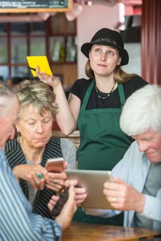 Mature friends in a coffee house distracted by their devices as server waits