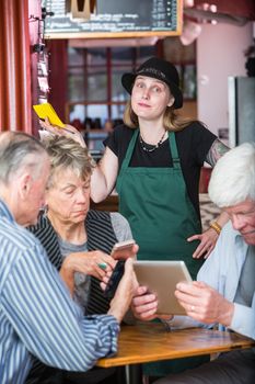Friends in a coffee house distracted by their devices as server waits