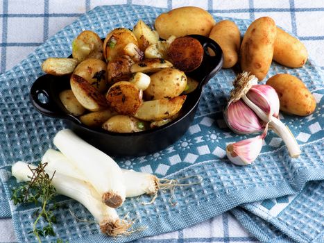 Homemade Roasted Potato Wedges and Halves in Black Cast Iron Pot with Fresh Raw Onion and Garlic closeup on Blue and Checkered Napkin