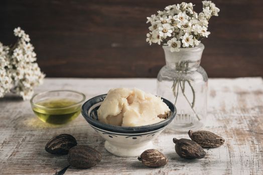 Two bowl of shea butter and oil with shea nuts on shabby wooden table.