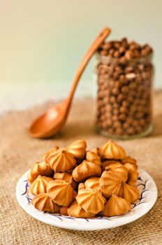 Small cookies on a plate and burlap. Bank with chocolate balls in the background and a wooden spoon, warm light and bokeh. A gradient background.