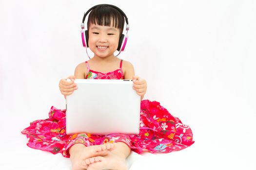 Chinese little girl on headphones holding tablet in plain isolated white background.