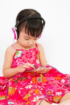 Chinese little girl on headphones holding mobile phone in plain isolated white background.