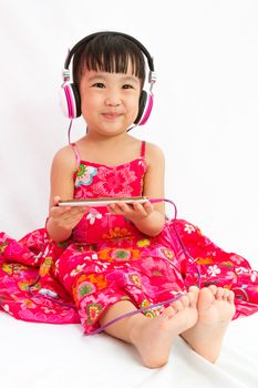 Chinese little girl on headphones holding mobile phone in plain isolated white background.