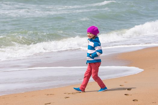 Happy girl walking along coastal sea beach on a warm spring day