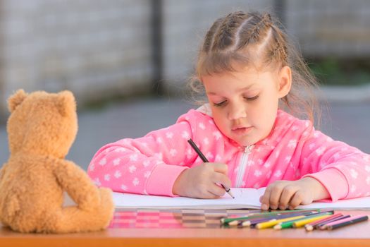 The girl with enthusiasm draws with crayons in the album