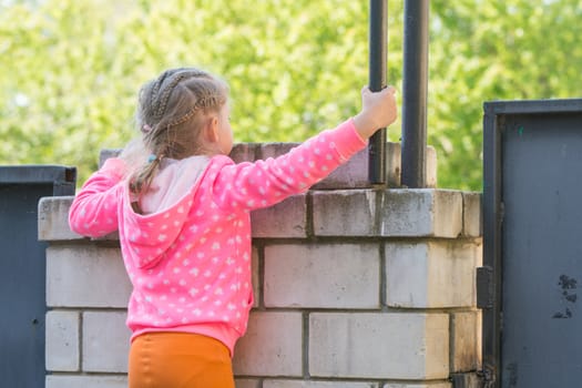 Five-year girl climbed on a brick fence and looks for him