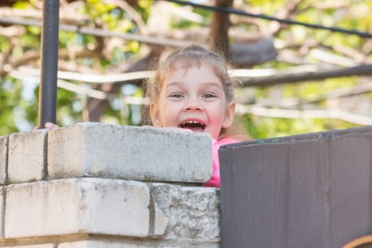 Five-year girl smiling looked out from behind the wall