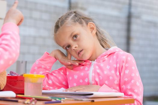 Girl sits thoughtfully at the table with accessories for painting