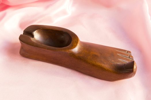decorative wooden ashtray in the shape of the foot on a pink silk