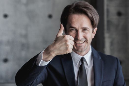 Portrait of businessman in suit showing thumb up sign over concrete wall background