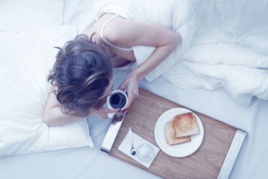 Beautiful young woman having breakfast in bed