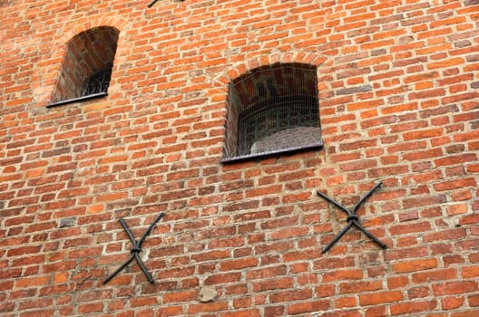 Small barred window in an old brick wall. The metal bars of the window in the form of an arch