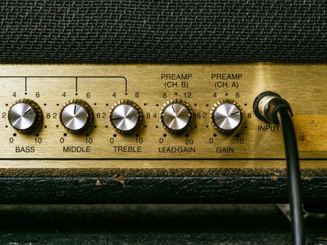 Macro photo of a vintage electric guitar amplifier showing the knobs and input plug.
