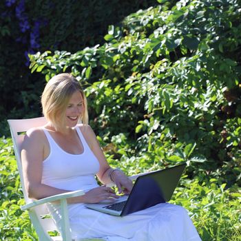 Woman working on a laptop outdoors in summer garden
