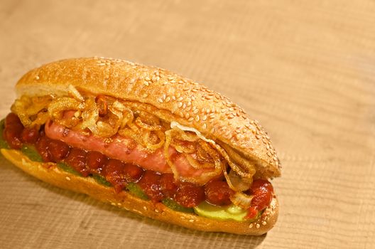 Hot dog with pickles, ketchup and grilled onions, laying on a Board. Warm color and bokeh.