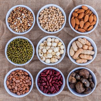 Mixed beans , lentils and nuts in the white bowl on brown cloth sack  background. mung bean, groundnut, soybean, red kidney bean , lotus seed ,almond,green bean,millet,cashew and brown pinto beans .