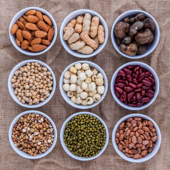 Mixed beans , lentils and nuts in the white bowl on brown cloth sack  background. mung bean, groundnut, soybean, red kidney bean , lotus seed ,almond,green bean,millet,cashew and brown pinto beans .