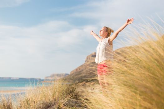 Relaxed woman, arms rised, enjoying sun, freedom and life an a beautiful beach. Young lady feeling free, relaxed and happy. Concept of vacations, freedom, happiness, enjoyment and well being.