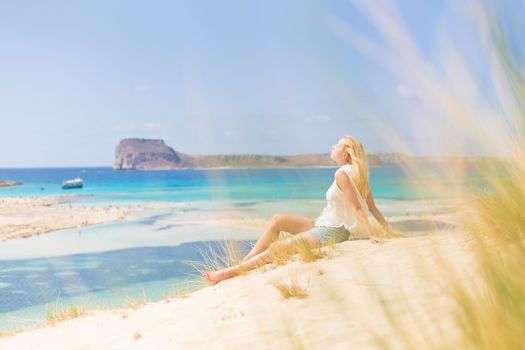 Relaxed woman enjoying sun, freedom and life an a beautiful sandy beach of Balos in Greece. Young lady feeling free, relaxed and happy. Vacations, freedom, happiness, enjoyment and well being.