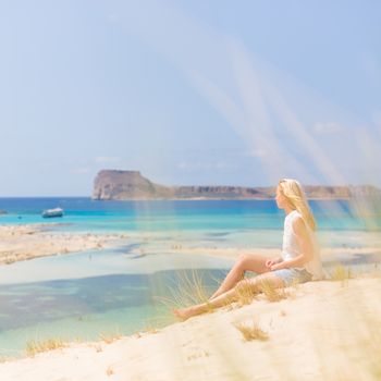 Relaxed woman enjoying sun, freedom and life an a beautiful sandy beach of Balos in Greece. Young lady feeling free, relaxed and happy. Vacations, freedom, happiness, enjoyment and well being.