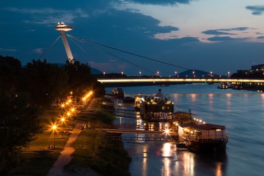 View on the Bridge of Slovak National Uprising (or UFO bridge). River Danube with reflections. Cloudy sunset sky.