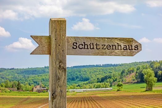 Signpost labeled with rifle associations clubhouse - in german language (Schuetzenhaus) - rural landscape in the background