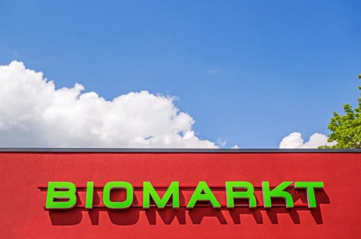 Bio market red facade labeled with "BIOMARKT", german language, blue sky with clouds