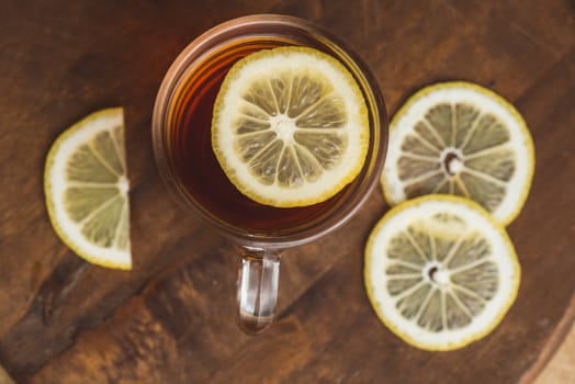 Top view of black tea with lemon in cup and on wooden plank table.