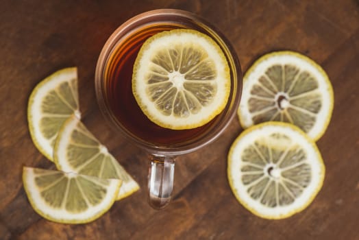 Top view of black tea with lemon in cup and on wooden plank table.